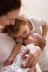 Elder sister kissing baby. Happy young mother holding baby